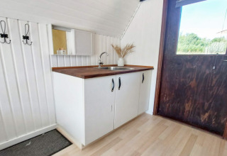 Piccolo angolo cottura con piano in legno, lavello e mobili bianchi in una casa vacanze a Hemmet, Danimarca.