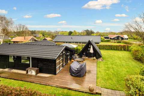 Vue extérieure d'une maison de vacances noire avec terrasse en bois et pelouse à Hemmet, Danemark.
