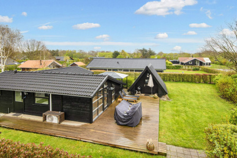 Buitenaanzicht van een zwart vakantiehuis met houten terras en groen gazon in Hemmet, Denemarken.