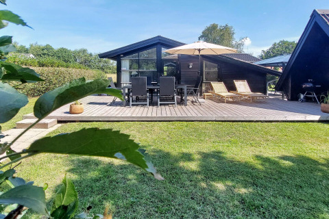 Træhytte med stor terrasse, havemøbler, solsenge og parasol i Hemmet, Danmark på en solrig dag.