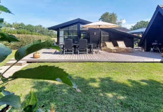Maison de vacances avec grande terrasse, transats, coin repas et parasol à Hemmet, Danemark.