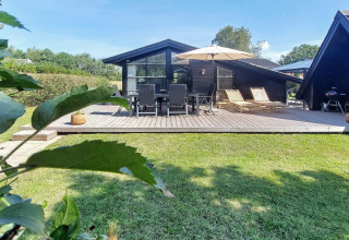 Træhytte med stor terrasse, havemøbler, solsenge og parasol i Hemmet, Danmark på en solrig dag.