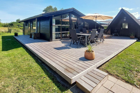 Udendørs terrasse ved seks-personers feriehus i Hemmet, Danmark, med havemøbler og parasol.
