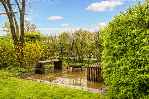Coin jardin avec deux bancs et un foyer sur dalles, entouré de verdure près d’un gîte à Hemmet, Danemark.
