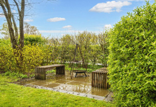 Coin jardin avec deux bancs et un foyer sur dalles, entouré de verdure près d’un gîte à Hemmet, Danemark.