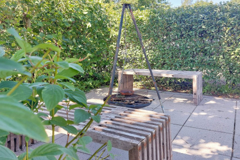 Buiten zitgedeelte met vuurplaats, houten banken en groen bij vakantiehuis in Hemmet, Denemarken.