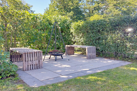 Buiten zitruimte met houten banken en vuurschaal, omringd door groen bij lodge in Hemmet, Denemarken.