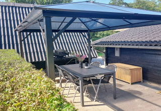 Espace repas extérieur couvert avec table noire et chaises chez maison de vacances à Hemmet, Danemark.
