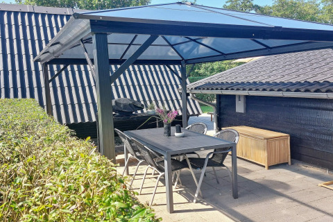 Overdekt terras met zwarte tafel, stoelen en barbecue bij vakantiewoning in Hemmet, Denemarken.