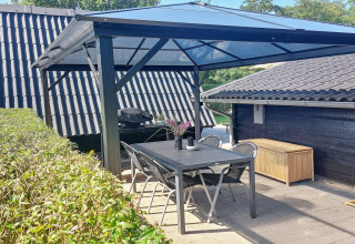 Overdekte eethoek buiten met tuintafel en stoelen bij vakantiehuis in Hemmet, Denemarken.