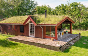 Casa vacanze rossa con tetto erboso e terrazza in legno a Roslev, Danimarca, immersa nel verde.