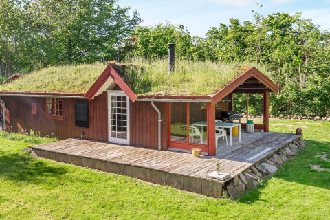 Casa vacanze rossa con tetto erboso e terrazza in legno a Roslev, Danimarca, immersa nel verde.