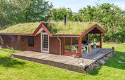 Casa vacanze rossa con tetto erboso e terrazza in legno a Roslev, Danimarca, immersa nel verde.