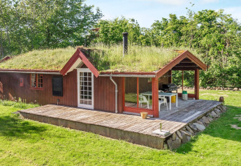 Rood houten vakantiehuis met grasdak en terras in Roslev, Denemarken, omgeven door veel groen.