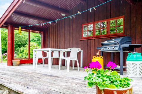 Porche de madera con mesa, sillas, parrilla y flores en una casa de vacaciones en Roslev, Dinamarca.