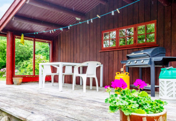 Houten veranda met tafel, stoelen, barbecue en bloemen bij een vakantiehuis in Roslev, Denemarken.