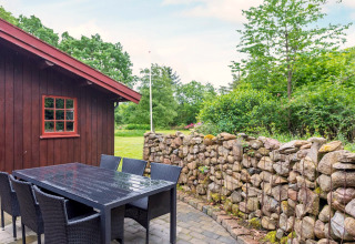 Espace repas extérieur du gîte 6 personnes à Roslev, Danemark, avec mur en pierres et cabane en bois.