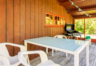 Espace repas extérieur d'un gîte à Roslev, Danemark, avec table en verre, chaises blanches et barbecue.
