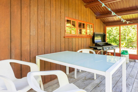 Espace repas extérieur d'un gîte à Roslev, Danemark, avec table en verre, chaises blanches et barbecue.