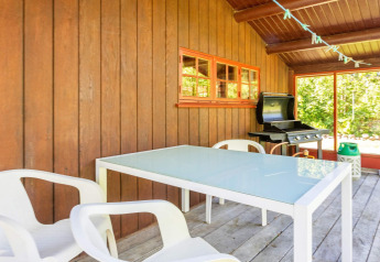 Overdekt terras bij een vakantiehuis in Roslev, Denemarken, met tuintafel, witte stoelen en barbecue.