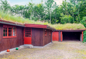 Rødt træhus med græstag og garage, omgivet af skov, fotograferet ved ferieboligen i Roslev, Danmark.