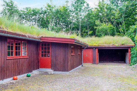 Casa in legno rossa con tetto erboso e garage, circondata da alberi, presso una casa vacanze a Roslev, Danimarca.