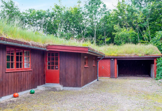 Casa de madera roja con techo de césped y garaje, rodeada de árboles, en una casa de vacaciones en Roslev, Dinamarca.