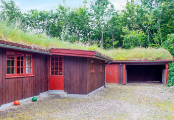 Rode houten woning met grasdak en garage, omringd door bomen bij een vakantiehuis in Roslev, Denemarken.