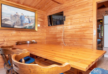 Wood-paneled dining area with painting, wall-mounted TV, wooden table and chairs in Roslev lodge, Denmark.