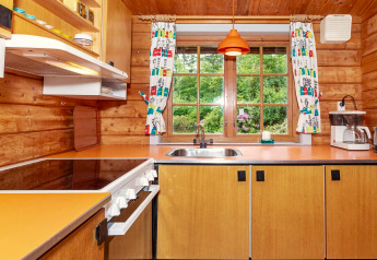 Gemütliche Holzküche mit orangefarbener Arbeitsplatte, Herd und Blick auf grünen Garten durch Fenster.