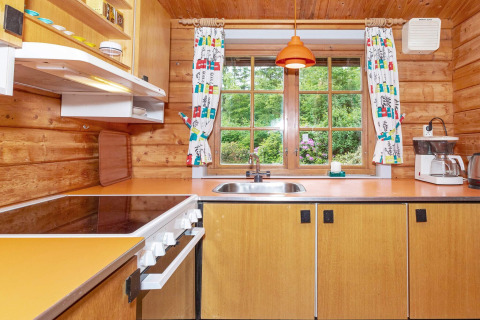 Gezellige houten keuken met oranje aanrecht, fornuis en groot raam met uitzicht op de groene tuin.