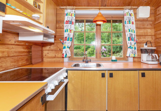 Gezellige houten keuken met oranje aanrecht, fornuis en groot raam met uitzicht op de groene tuin.