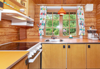 Gemütliche Holzküche mit orangefarbener Arbeitsplatte, Herd und Blick auf grünen Garten durch Fenster.