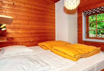 Gemütliches Schlafzimmer mit Holzverkleidung, gelber Bettdecke und Fenster in einem Ferienhaus Roslev.