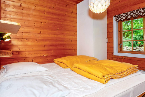 Chambre chaleureuse avec murs en bois, couettes jaunes et fenêtre, dans une maison de vacances à Roslev, Danemark.