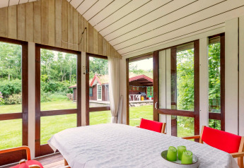 Lys spisestue i sommerhus i Roslev, Danmark, med store vinduer og udsigt til have og udhus.