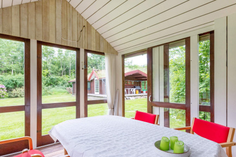 Lichte eetruimte in vakantiehuis in Roslev, Denemarken, met zicht op tuin en rode stoelen.
