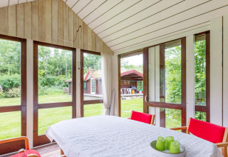 Lys spisestue i sommerhus i Roslev, Danmark, med store vinduer og udsigt til have og udhus.