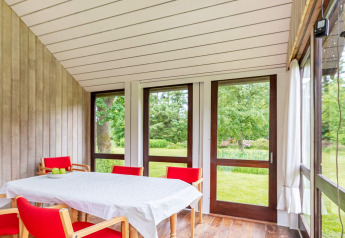 Licht vakantiehuis in Roslev, Denemarken met eethoek, rode stoelen en uitzicht op de groene tuin door ramen.