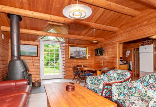 Salon en bois chaleureux avec poêle, chaises fleuries et coin repas dans maison de vacances à Roslev, Danemark.