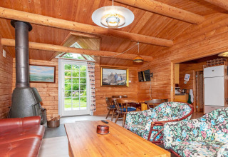 Salon en bois chaleureux avec poêle, chaises fleuries et coin repas dans maison de vacances à Roslev, Danemark.