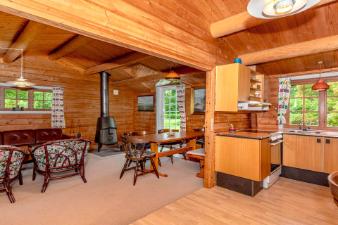 Salon et cuisine en bois chaleureux du « gîte 6 personnes à Roslev » au Danemark, avec poêle et fenêtres.