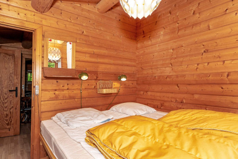 Schlafzimmer einer Blockhütte mit Doppelbett, gelber Decke und Holzinterieur im Ferienhaus Roslev.