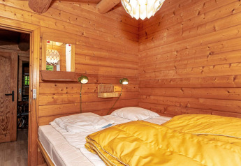 Slaapkamer in houten lodge met tweepersoonsbed, gele donsdeken en wandlampen in vakantiehuis Roslev, Denemarken.