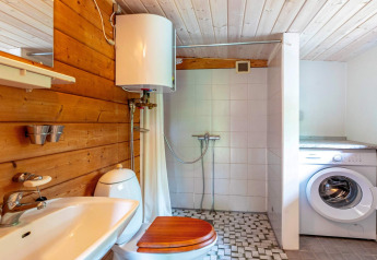Badkamer met houten en betegelde muren, douche, wasmachine en boiler in Roslev, Denemarken.