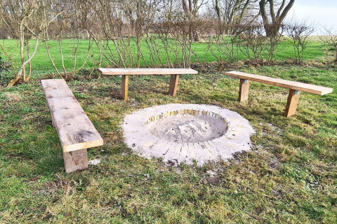 Feuerstelle mit drei Holzbänken im Grünen nahe einem 5-Sterne-Ferienhaus in Sydals, Dänemark.