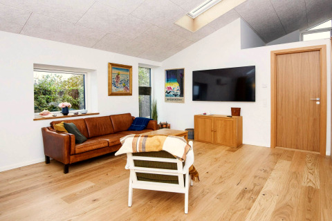 Salon à la décoration moderne, canapé en cuir, œuvres murales, grande TV et parquet dans un lodge à Sydals.