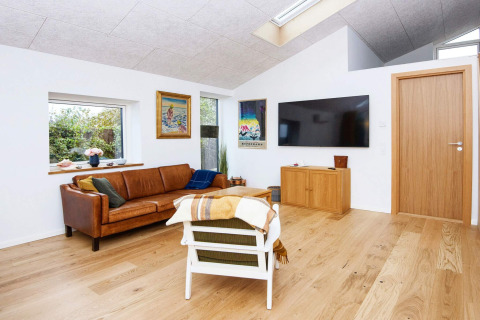 Salon à la décoration moderne, canapé en cuir, œuvres murales, grande TV et parquet dans un lodge à Sydals.