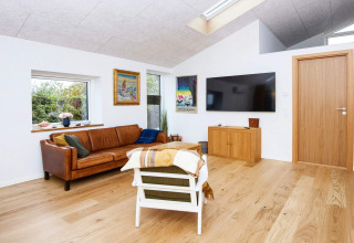 Woonkamer met modern interieur, lederen zetel, muurkunst, grote tv en houten vloer in lodge in Sydals.