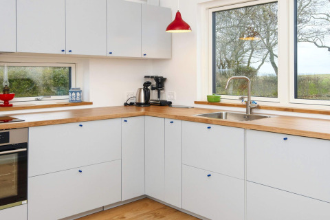 Cuisine moderne avec plan de travail en bois, armoires blanches et grandes fenêtres dans une maison de vacances 5 étoiles à Sydals, Danemark.